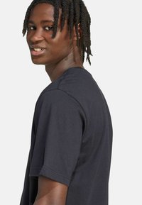 Černé tričko s krátkým rukávem vyrobené z měkké bavlny, s klasickým výstřihem a volným střihem. Hladká textura s podrobným šitím podél švů.