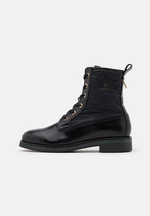 Bottine noire en cuir et tissu matelassé avec fermeture à lacets devant, œillets dorés, logo latéral et languette à l'arrière.