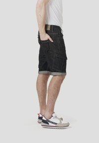 Shorts en jean noir avec un ourlet retroussé, dotés de poches latérales et d'une coupe décontractée, associés à des baskets sportives multicolores.