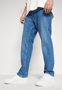 Ljust blå jeans med rak passform, med synliga sömmar och sidofickor, tillsammans med vita sneakers.