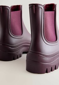 Bottes en caoutchouc bourgogne à chevilles avec des panneaux latéraux élastiques, des semelles texturées et un talon épais. Comprend une doublure intérieure douce.