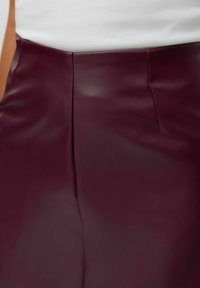Falda de cuero sintético burdeos con una textura suave, que presenta una cintura alta y costuras sutiles a lo largo de las costuras para un ajuste estructurado.