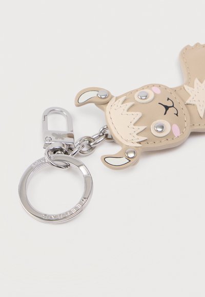Μπρελόκ με σχέδιο λάμα από μπεζ δέρμα, με ασημένιο εξάρτημα, μαύρες και ροζ λεπτομέρειες και στεφάνι δακτυλίου για στερέωση.