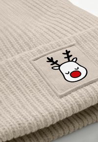Beige knitted beanie hat featuring a square patch with a cartoon reindeer face, complete with antlers and a red nose.