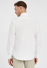 Witte overhemd met lange mouwen, voorzien van een klassieke kraag, knoopmanchetten en een afgeronde zoom. De stof lijkt soepel en licht van gewicht.