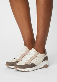 Zapatillas blancas y beige con acentos marrones, de cuero texturizado y tejido, con un diseño perforado, puntera redonda y suela de contraste.