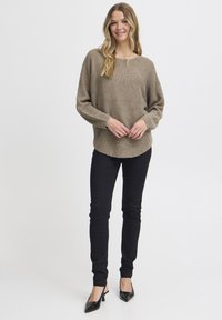 Hellbrauner Strickpullover mit lockerem Schnitt und gerippter Textur, kombiniert mit schwarzen Skinny-Jeans und schwarzen spitzen Pumps.