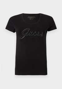 Black cotton t-shirt with short sleeves and a round neckline. Features a glossy "Guess" logo in rhinestones across the front.