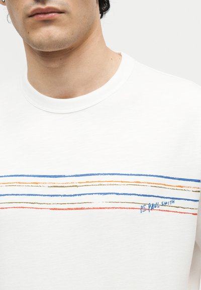 Νέος άντρας που φοράει λευκό πουκάμισο με οριζόντιες μπλε, πορτοκαλί και μπεζ ρίγες και το κείμενο "PS Paul Smith" στο στήθος.