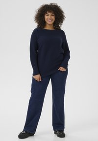 Navy ribbed knit sweater with long sleeves and a wide neckline, paired with dark blue straight-leg jeans and black platform shoes.