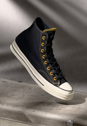 High-top sneaker in donkerblauw canvas met gele veteroogjes, zwarte veters en een witte rubberen neuskap; met contrasterende gele stiksels.