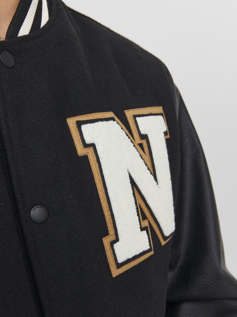 Chaqueta varsity negra con mangas de cuero y un gran parche en forma de letra "N" blanca contorneado en beige en el pecho.