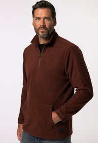 Brun fleece pullover med halv lynlås, lange ærmer og frontlomme. Har en tekstureret overflade og et lille logo på kanten.