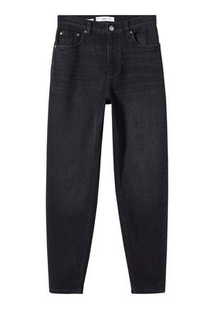 Person iført en hvid og sort stribet sweater over en lyseblå skjorte, stoppet ned i højtaljede sorte bukser med hænderne i lommerne.