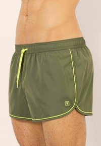 Olivgröna badshorts i lättviktsmaterial, med dragsko i midjan, kontrasterande neongul piping och logodetalj.