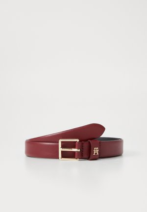 Cinturón de cuero burdeos con hebilla rectangular dorada y logo grabado. Presenta una textura suave y un diseño tapered.