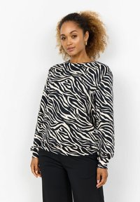 Zebra print sweatshirt in cream and black, featuring a round neckline, long sleeves, and soft fabric. Paired with black pants.