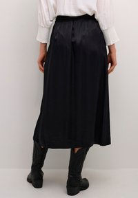 Zwarte satijnen lange rok met een gladde textuur en een elastische tailleband, gecombineerd met zwarte cowboylaarzen met gedetailleerde stiksels.