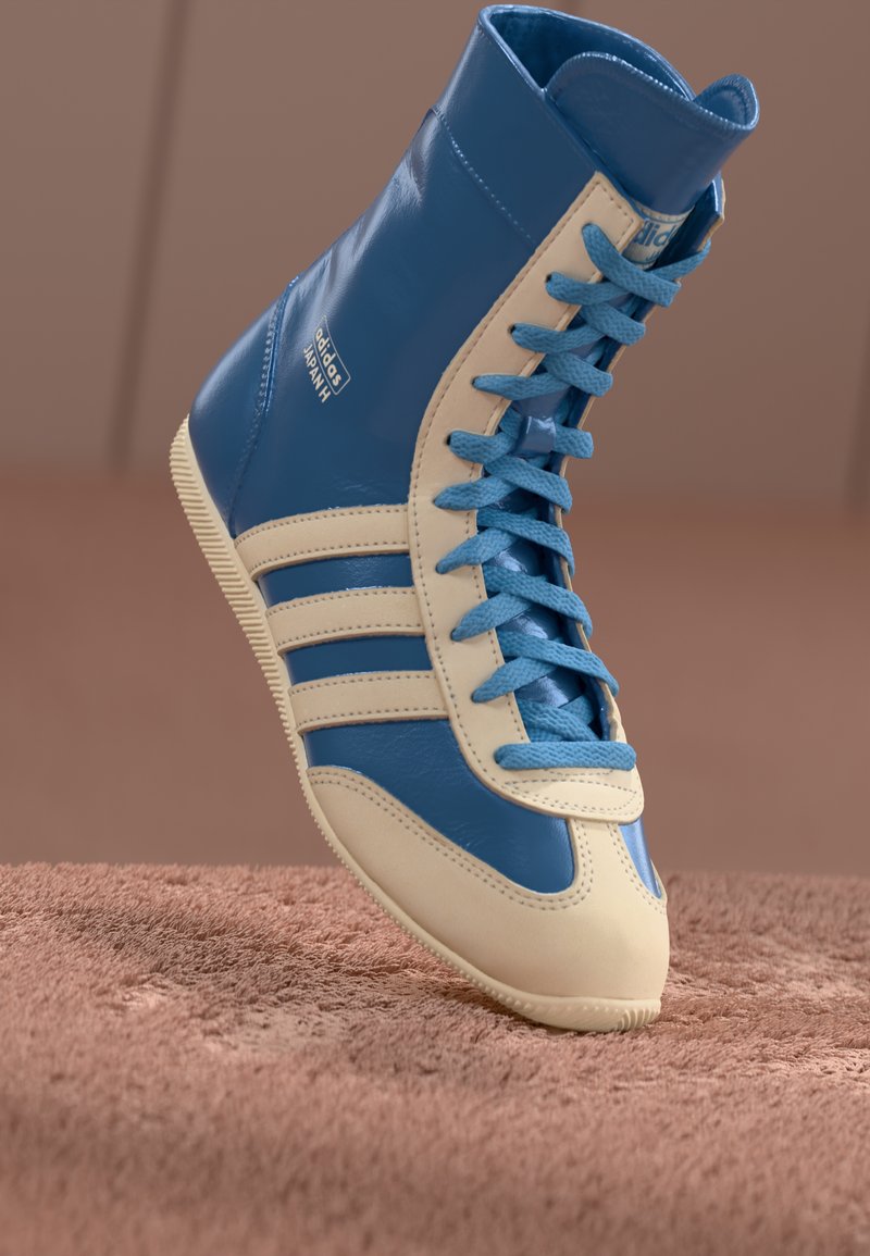 Zapatilla alta en cuero azul y crema, con una suela texturizada, cordones en contraste y tres franjas características en el lateral.