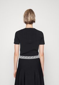 Maglietta nera a maniche corte con scollatura a girocollo e zip sul retro, abbinata a una gonna nera con vita brandizzata bianca.