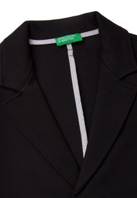 Czarny żakiet z klapami, z białą podszewką i zieloną metką z napisem "United Colors of Benetton". Gładka tekstura.