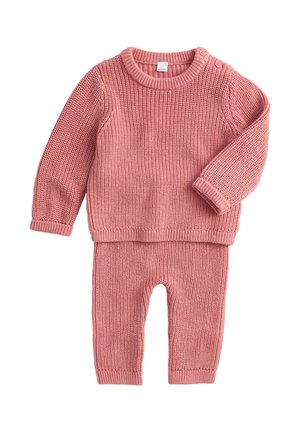 Różowy sweter z dzianiny i dopasowany zestaw spodni. Sweter ma długie rękawy i okrągły dekolt, ozdobiony guzikami na jednym ramieniu.