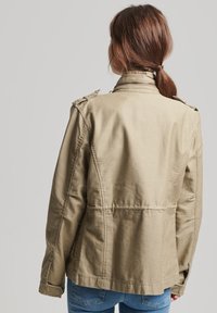 Khaki bawełniana kurtka z stójką, pagonami i dopasowanym krojem. Charakteryzuje się gładką fakturą i lekko usztywnionym fasonem.