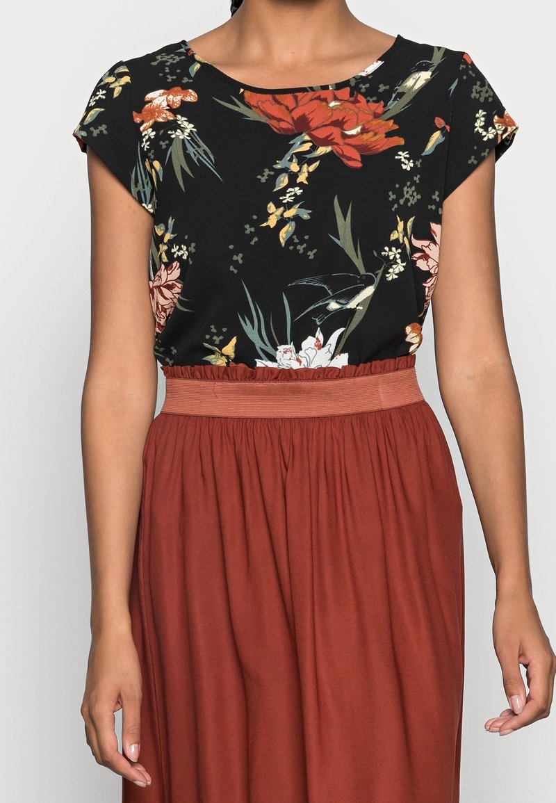 Haut à imprimé floral sur un tissu noir, avec un col rond et des manches courtes, associé à une jupe fluide de couleur rouille à taille élastique.