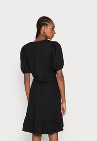 Vestido preto até ao joelho com mangas bufantes, bainha com volantes e um decote simples. Feito de um tecido suave e leve.