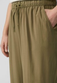 Olivengrüne, leichte Hose mit elastischem Bund, Kordelzug und seitlichen Taschen. Glatte Textur mit einer lockeren Passform.