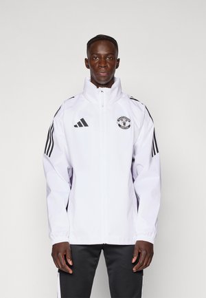 Witte zip-up jas met een hoge kraag, Adidas-logo, Manchester United badge en zwarte strepen op de mouwen. Gladde textuur, atletische pasvorm.
