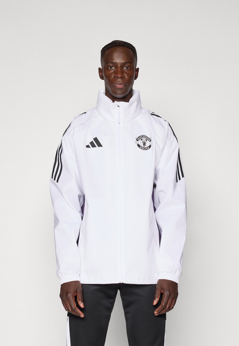 Witte zip-up jas met een hoge kraag, Adidas-logo, Manchester United badge en zwarte strepen op de mouwen. Gladde textuur, atletische pasvorm.