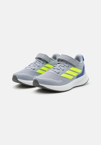 Baskets de sport grises avec des accents jaunes néon, tige en maille, sangle velcro ajustable et semelle rembourrée pour le soutien et le confort.