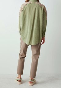 Grønstribet skjorte med hæklede detaljer på skuldrene, parret med beige bukser og sandaler med grønne blomster mønstre.
