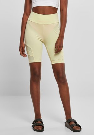 Hoge taille, lichtgele fietsbroek met een gladde textuur en zijzakken, gecombineerd met donkere sandalen.