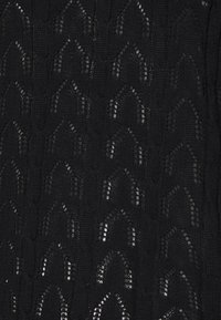 Czarna dzianina z wyraźnym wzorem łukowatych kształtów, o półprzezroczystej jakości i z żeberkowanymi detalami na całej powierzchni.