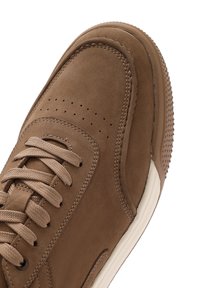 Sneaker in suede marrone con punta arrotondata e dettagli cuciti. Presenta perforazioni sulla parte anteriore e una suola in gomma testurizzata.