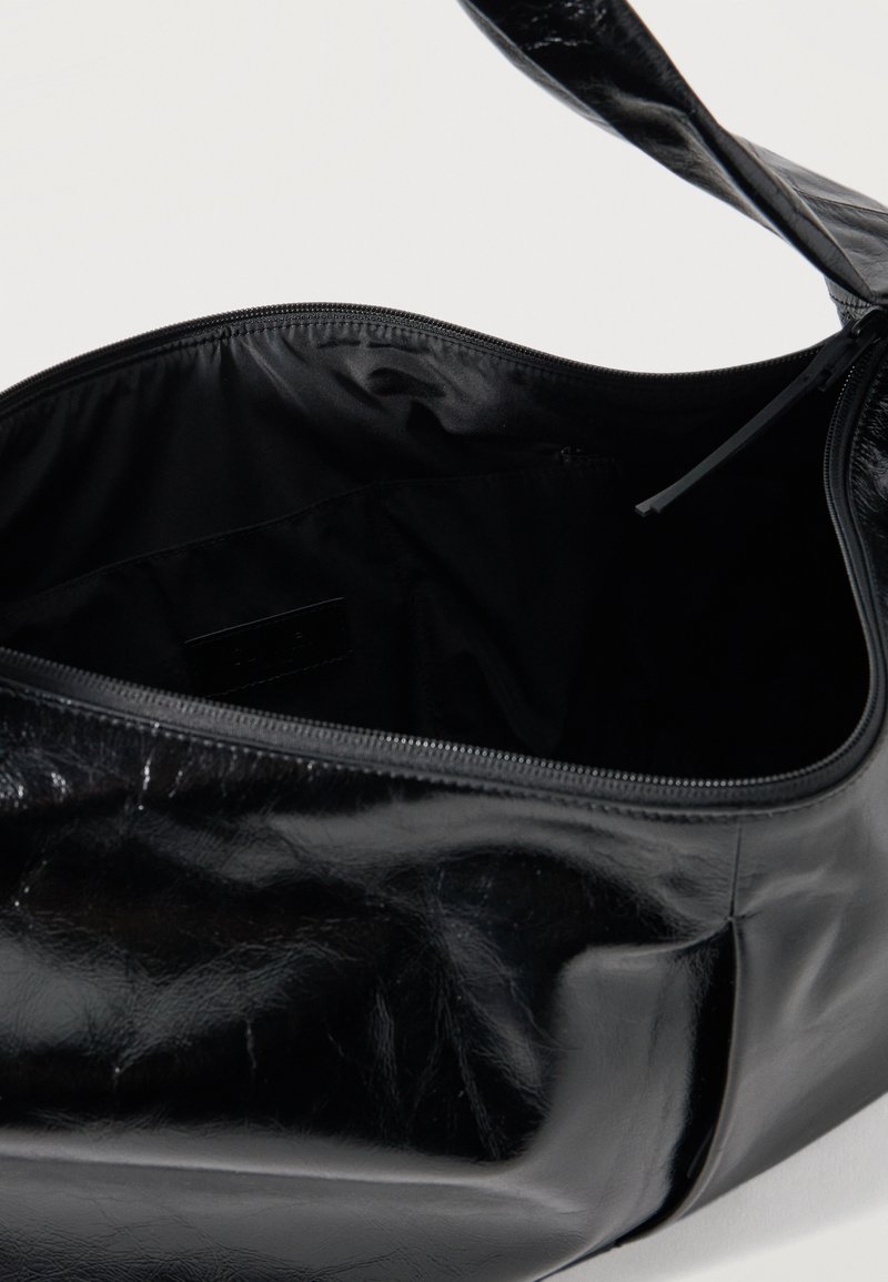 Sac bandoulière en cuir noir brillant avec un compartiment principal zippé ouvert, révélant une doublure intérieure en tissu noir lisse.