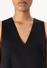 Black sleeveless top with a deep V-neck design, crafted from smooth fabric, featuring clean lines and a minimalist silhouette.