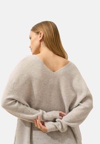 Lichtgrijze gebreide trui met een brede V-hals, geribbelde textuur, verlaagde schouders en lange mouwen, met omgeslagen manchetten en een relaxed fit.
