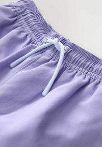 Levanduľové plavky s elastickým pásom, ktoré majú svetlomodrú šnúrku, hladkú tkaninu a prešitie.