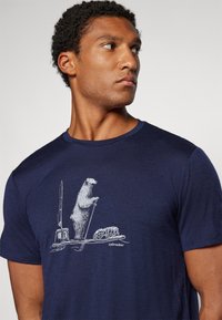 Camiseta de manga corta azul marino hecha de tela texturizada, con un gráfico blanco de un oso en una balsa improvisada con un remo y equipo.