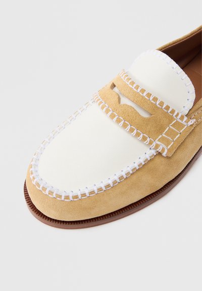 Ταμπά σουέτ μοκασίνι με λευκό δερμάτινο πάνελ, διακοσμητικό λευκό ραφτό σχέδιο και κοψίματα στο πάνω μέρος. Χαμηλή ελαστική σόλα.