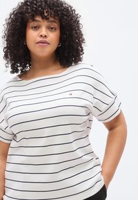 Λευκό ριγέ μπλουζάκι με οριζόντιες ναυτικές μπλε γραμμές, κοντά μανίκια, λαιμόκοψη καραβοπαναρισμένη και μικρό λογότυπο της μάρκας στην αριστερή πλευρά. Λείο βαμβακερό ύφασμα.