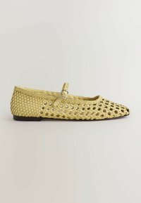 Chaussure plate jaune tissée avec bout pointu et bride à la cheville dotée d'une boucle argentée, présentée sur un fond clair uni.