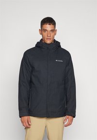 Veste à capuche noire en matériau résistant à l'eau, dotée d'une fermeture éclair à l'avant, de deux poches latérales et d'un logo Columbia sur la poitrine.