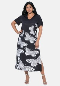 Schwarzes Kleid mit weißem Schmetterlingsmuster, kurzen Ärmeln, V-Ausschnitt und seitlichen Schlitzen. Hergestellt aus weichem Stoff; lockere Passform. Länge: knielang.