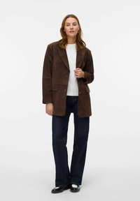Brun suedet blazer med to frontlommer, notched lapels og avslappet passform, kombinert med en hvit skjorte og mørke denimjeans.
