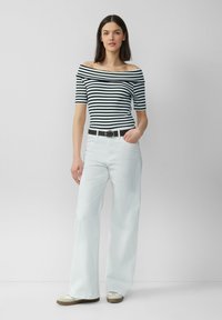 Schwarz-weiß gestreiftes Off-Shoulder-Oberteil, kombiniert mit hochtaillierten weißen weiten Hosen, versehen mit einem schwarzen Gürtel mit silberner Schnalle.
