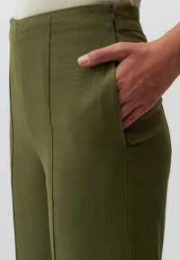 Pantalon en tissu léger vert olive avec une coupe décontractée, comportant des poches latérales et un discret detailing de coutures verticales.